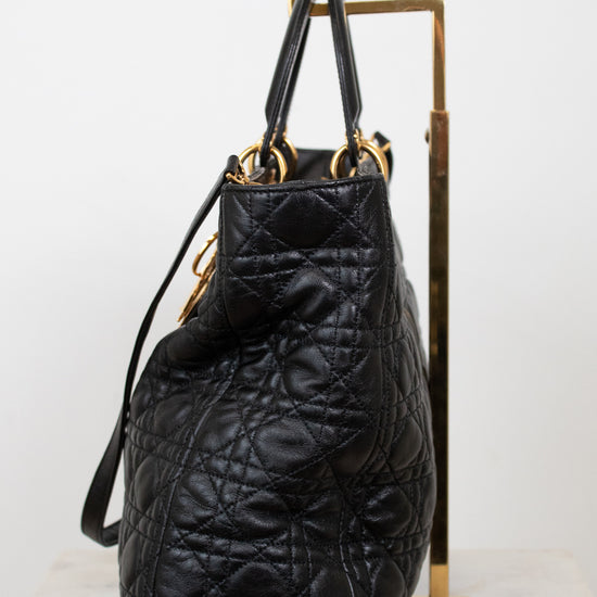 A black quilted leather handbag with gold-tone hardware, displayed on a gold metal stand against a white background.