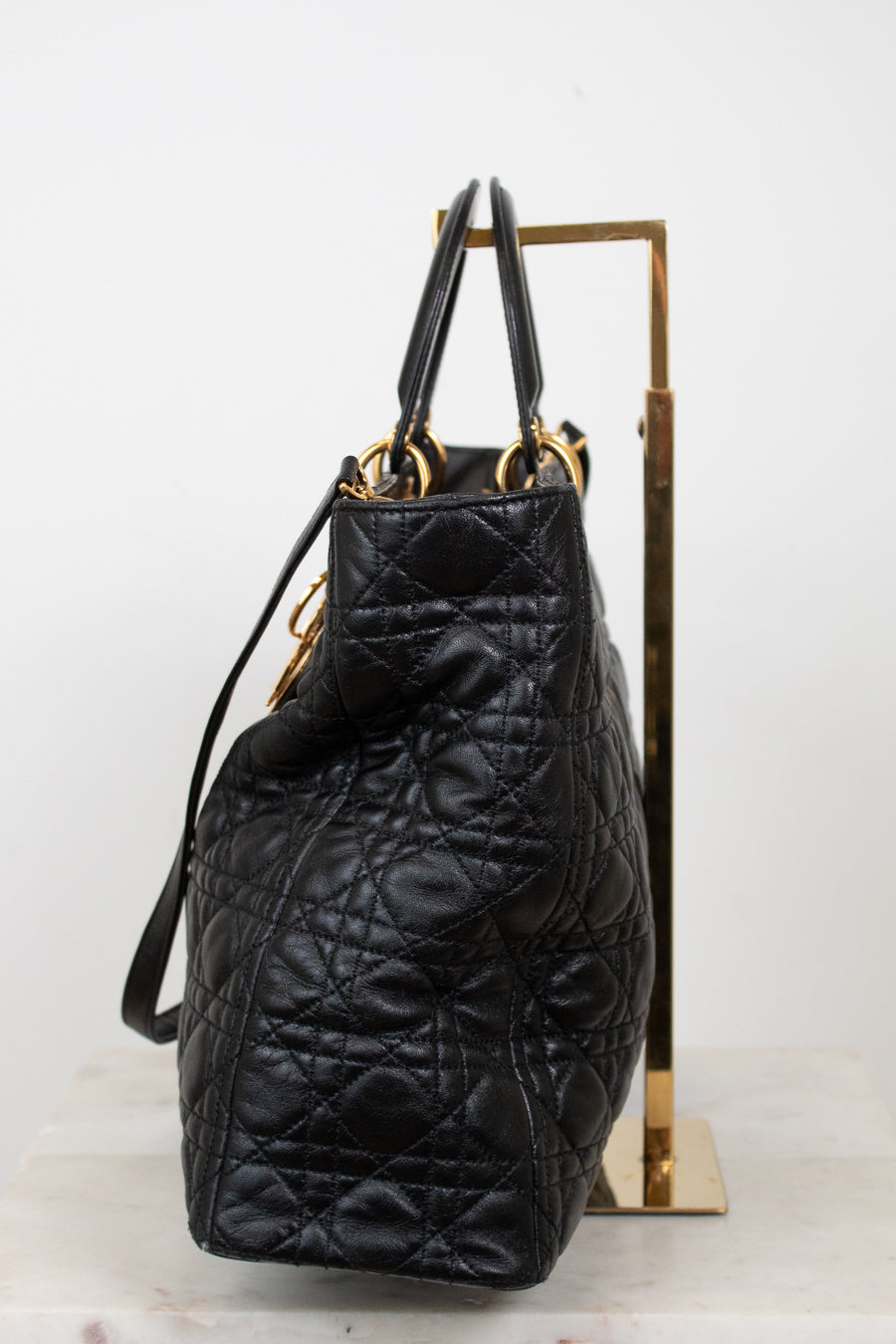 A black quilted leather handbag with gold-tone hardware, displayed on a gold metal stand against a white background.