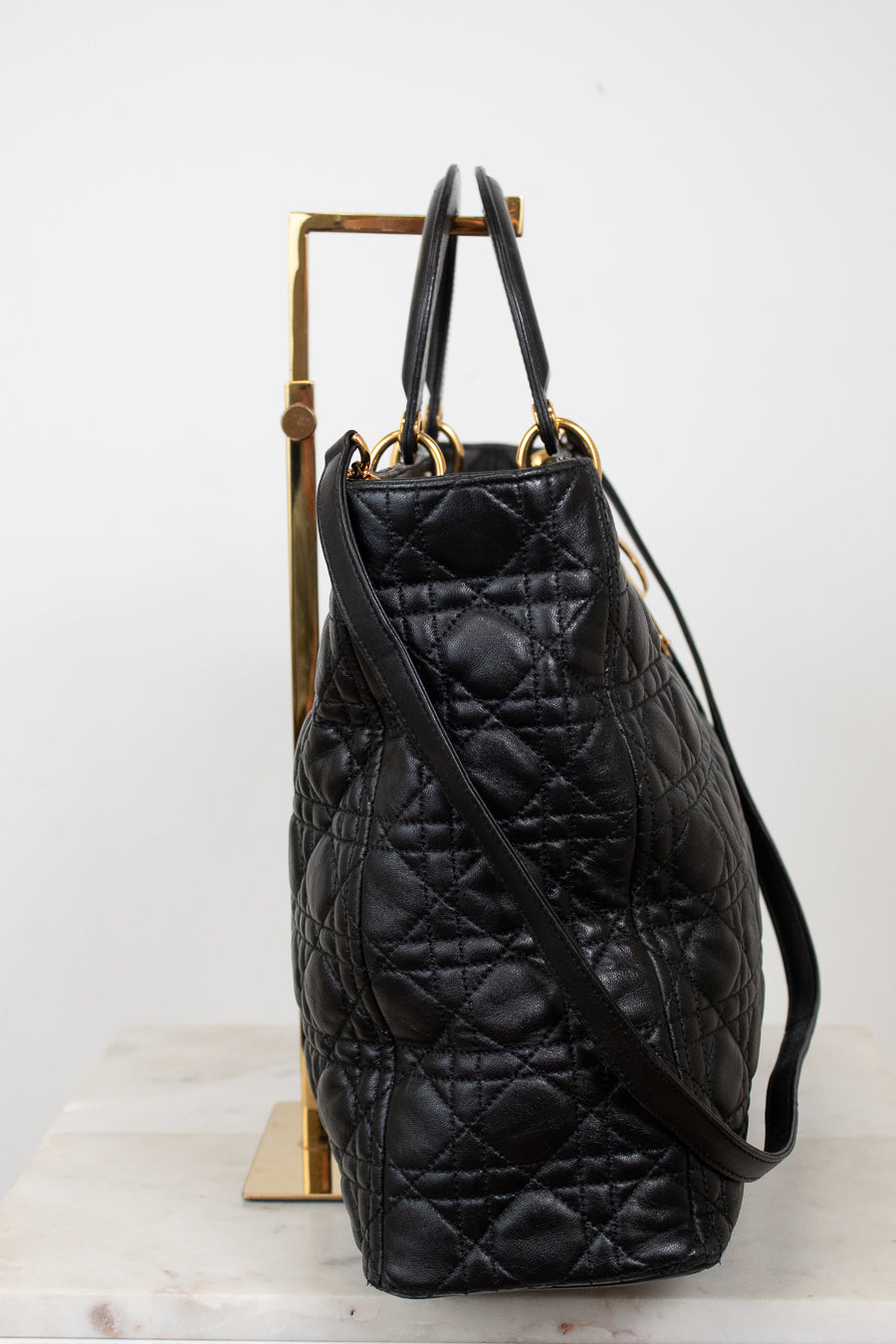 A black quilted leather handbag with gold-tone hardware, displayed on a gold stand against a white background.