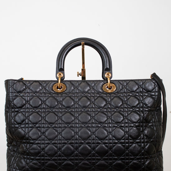 A black quilted leather top-handle satchel bag with gold-tone hardware, displayed on a white marble block against a white background.