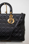 A black quilted leather top-handle handbag with gold-tone hardware, featuring a prominent interlocking 'D' charm and a thin shoulder strap, photographed against a light neutral background.