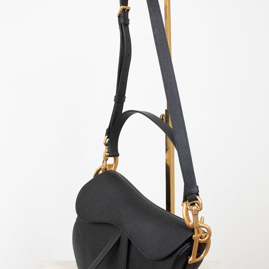 Black saddle bag with black straps on gold stand against a white background