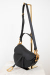 Black saddle bag with black straps on gold stand against a white background