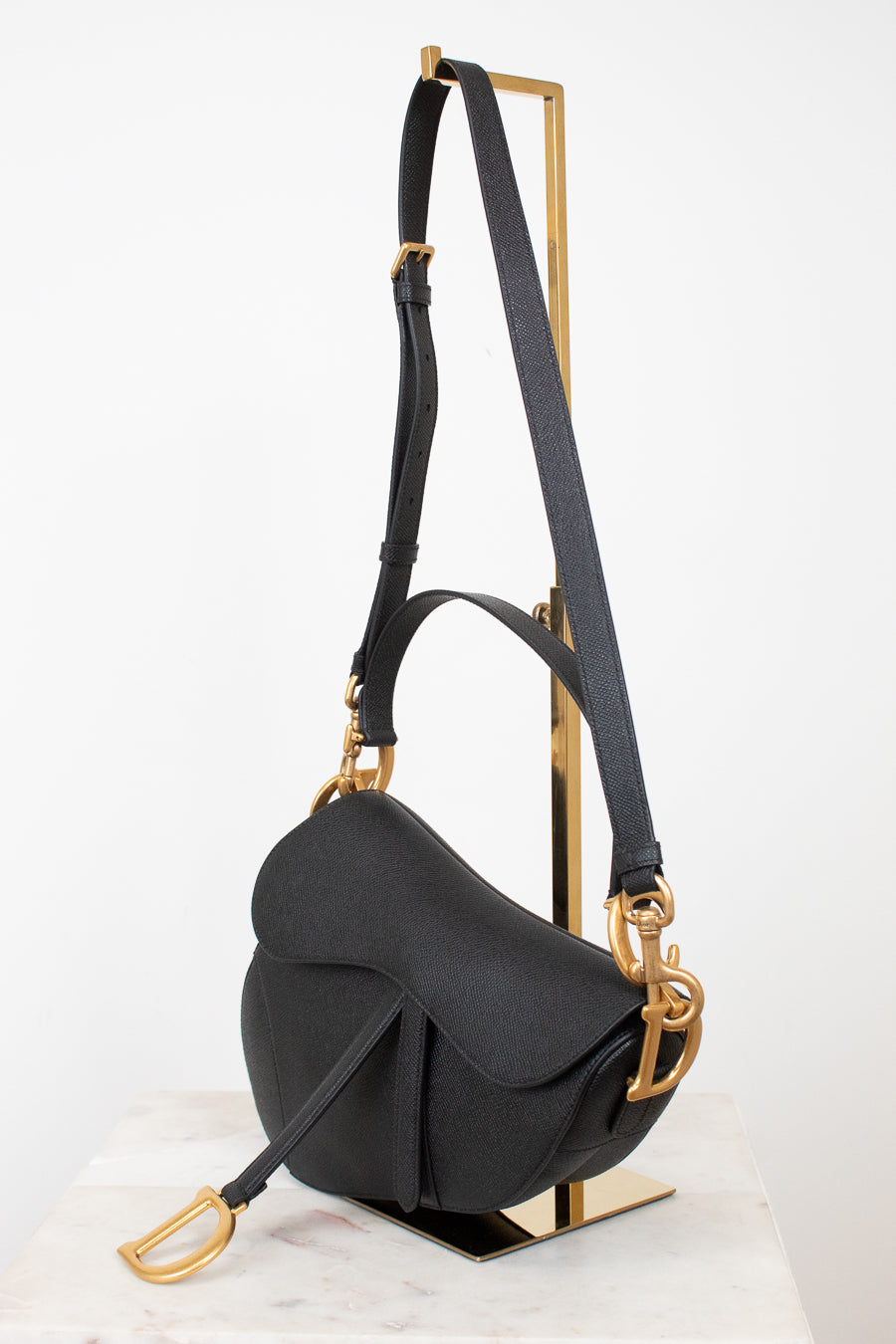 Black saddle bag with black straps on gold stand against a white background