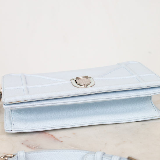 A light blue leather bag with a silver-tone clasp, displayed on a light marble surface with its matching strap in the foreground.