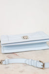 A light blue leather bag with a silver-tone clasp, displayed on a light marble surface with its matching strap in the foreground.