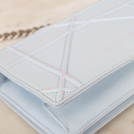 A light blue pebbled leather bag with geometric quilted stitched details, shown on a light marble surface with a silver-tone chain partially visible.