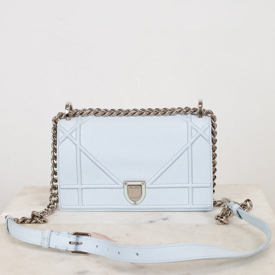 A light blue leather shoulder bag with a chain strap with matching light blue leather strap details, displayed on a marble surface against a white background.