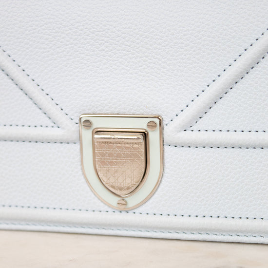 Close-up of a light blue pebbled leather handbag with a silver-tone clasp and stitched details, resting on a light marble surface.