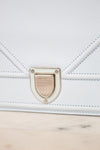 Close-up of a light blue pebbled leather handbag with a silver-tone clasp and stitched details, resting on a light marble surface.