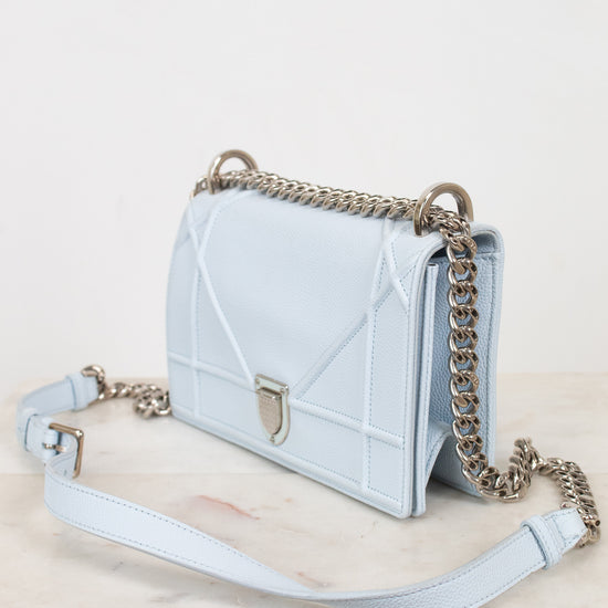 A light blue quilted leather shoulder bag with a silver-tone chain strap and a matching light blue shoulder strap, displayed on a light marble surface against a white background.