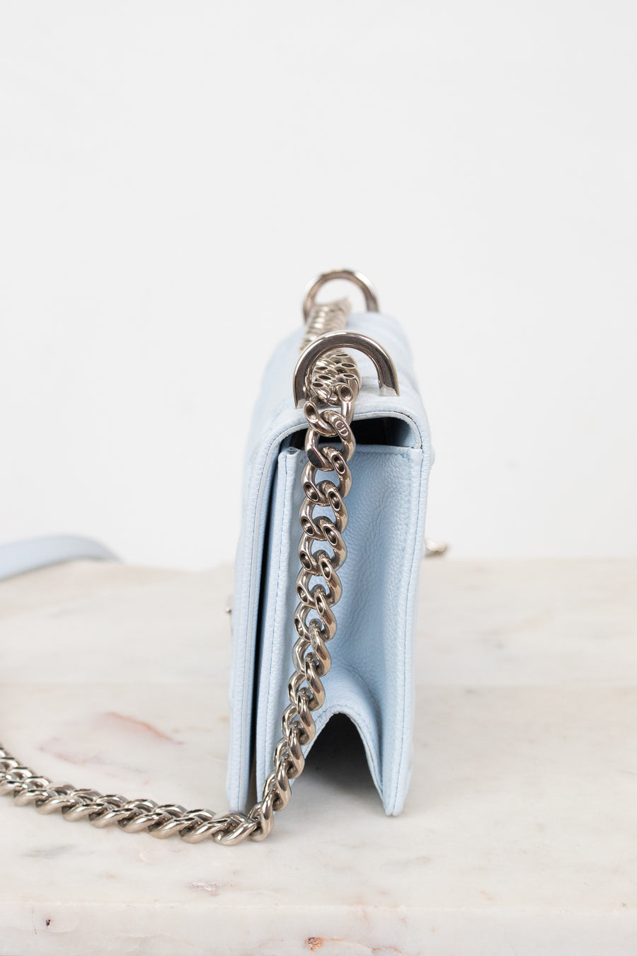 A light blue leather shoulder bag shown from the side, featuring a silver-tone chain strap and a silver-tone metal ring detail, set against a plain white background.