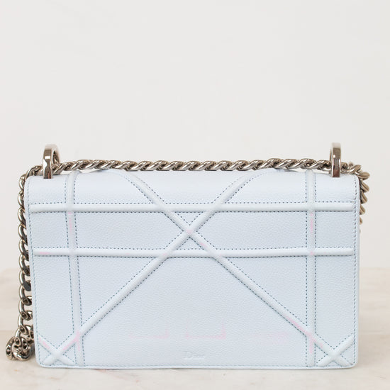 A light blue quilted leather shoulder bag with a geometric quilted pattern and a silver-tone chain strap, resting on a light marble surface against a plain off-white background.