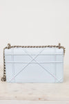 A light blue quilted leather shoulder bag with a geometric quilted pattern and a silver-tone chain strap, resting on a light marble surface against a plain off-white background.