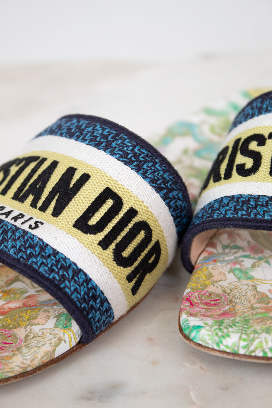 Close up of floral sandals with 'Christian Dior' strap on a marble surface