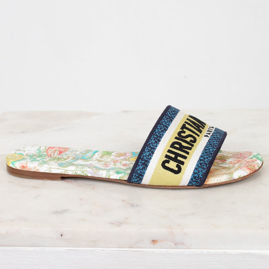 Side view of floral sandals with 'Christian Dior' blue/black/white/chartreuse strap on a marble surface