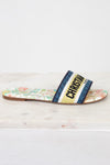 Side view of floral sandals with 'Christian Dior' blue/black/white/chartreuse strap on a marble surface