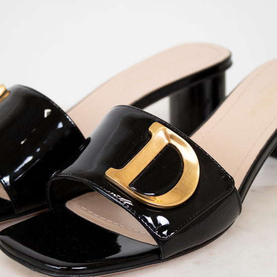 Black patent leather slide sandal with gold logo on a light background