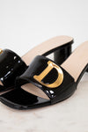 Black patent leather slide sandal with gold logo on a light background