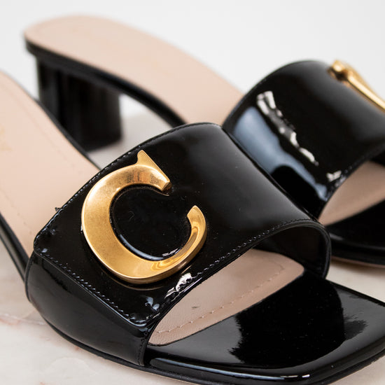 Black patent leather sandals with gold logo on a light background