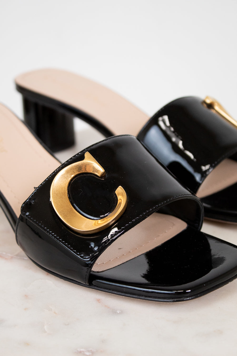 Black patent leather sandals with gold logo on a light background