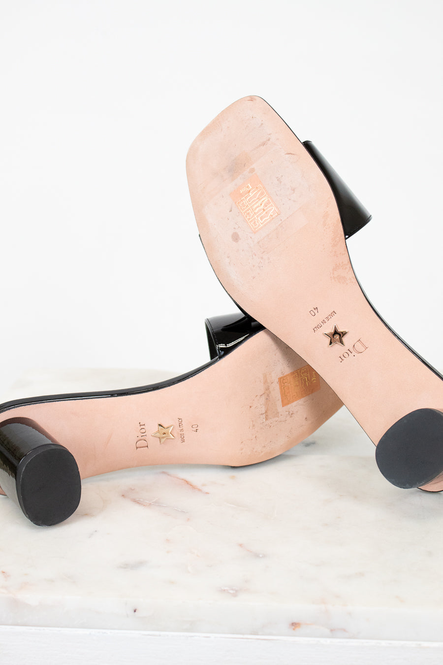 Soles of high-heeled shoes with visible brand names on a light background