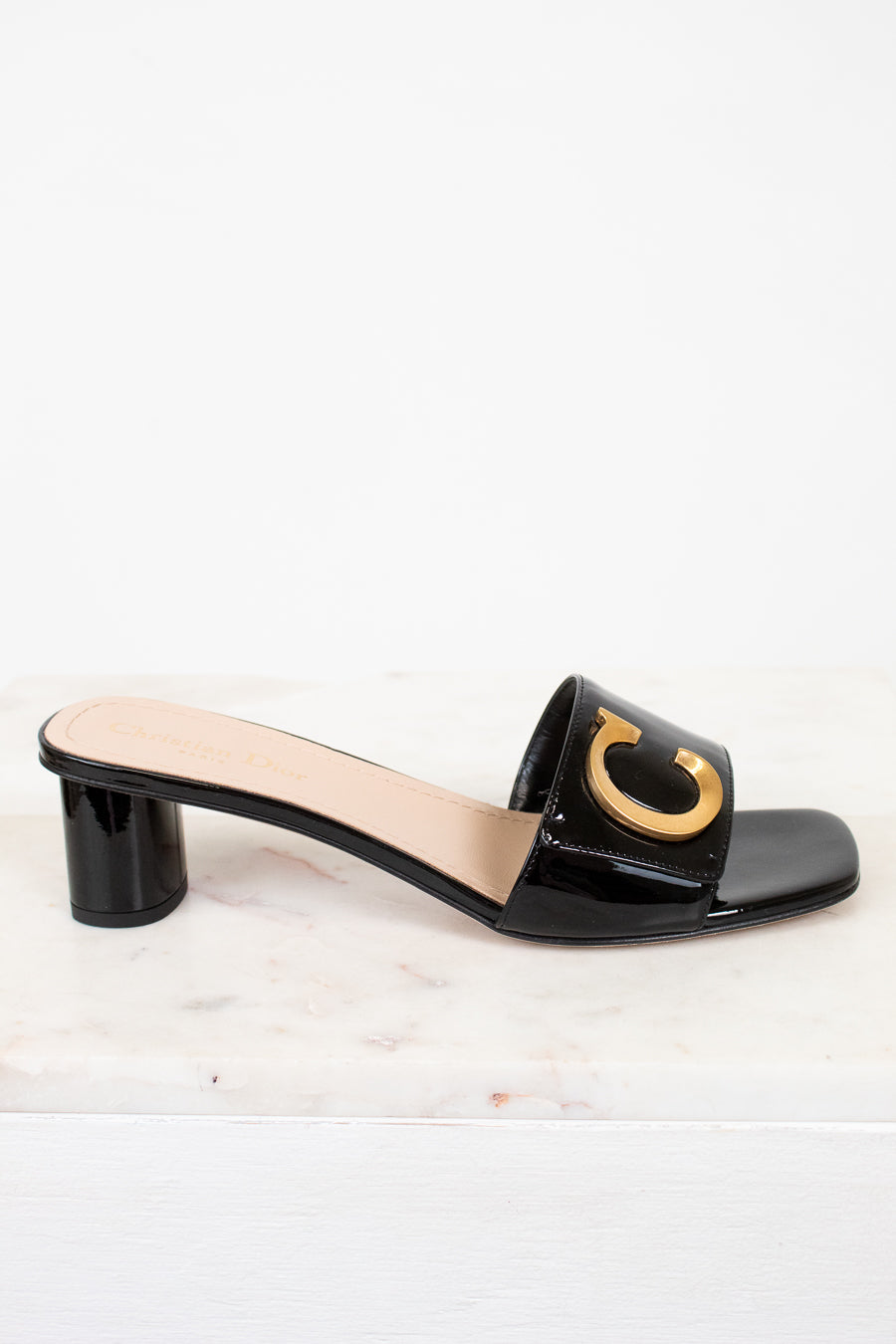 Black sandal with a gold 'C' design on a white background