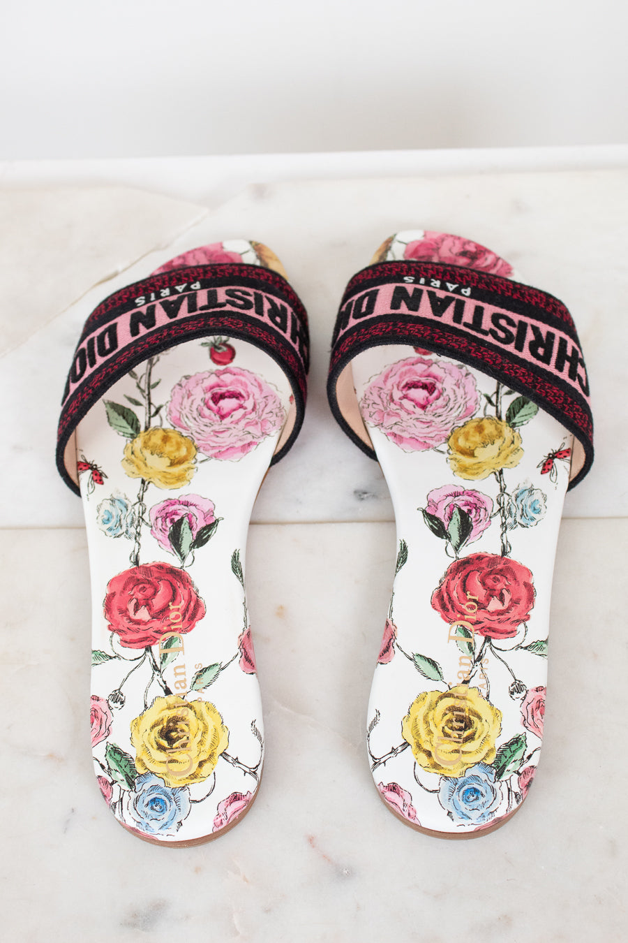 Floral flat sandals with Christian Dior in pink and black woven into toe strap on marble background