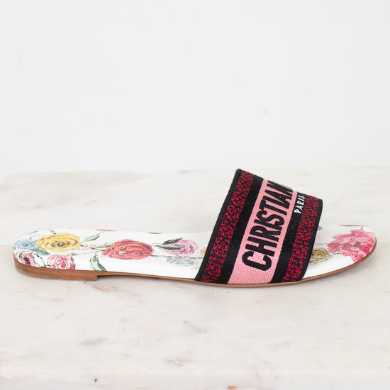 Side view of floral flat sandals with Christian Dior in pink and black woven into toe strap on marble background