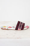 Side view of floral flat sandals with Christian Dior in pink and black woven into toe strap on marble background