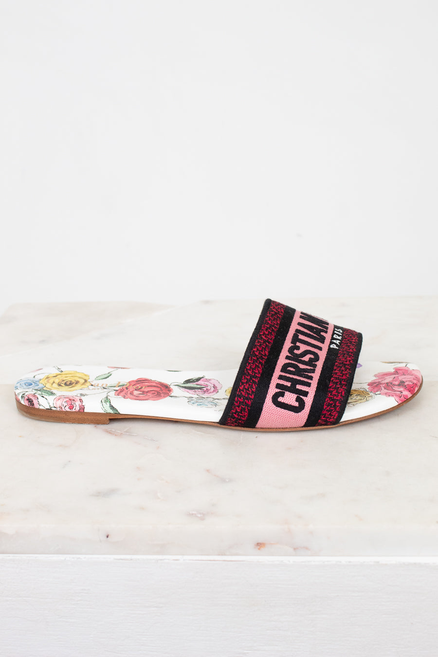 Side view of floral flat sandals with Christian Dior in pink and black woven into toe strap on marble background