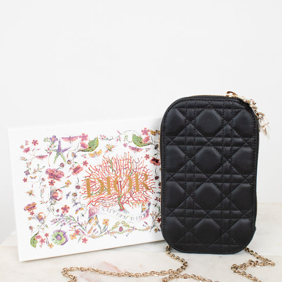 Black quilted handbag with gold chain on a white surface with a floral box.