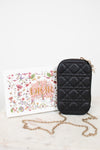 Black quilted handbag with gold chain on a white surface with a floral box.