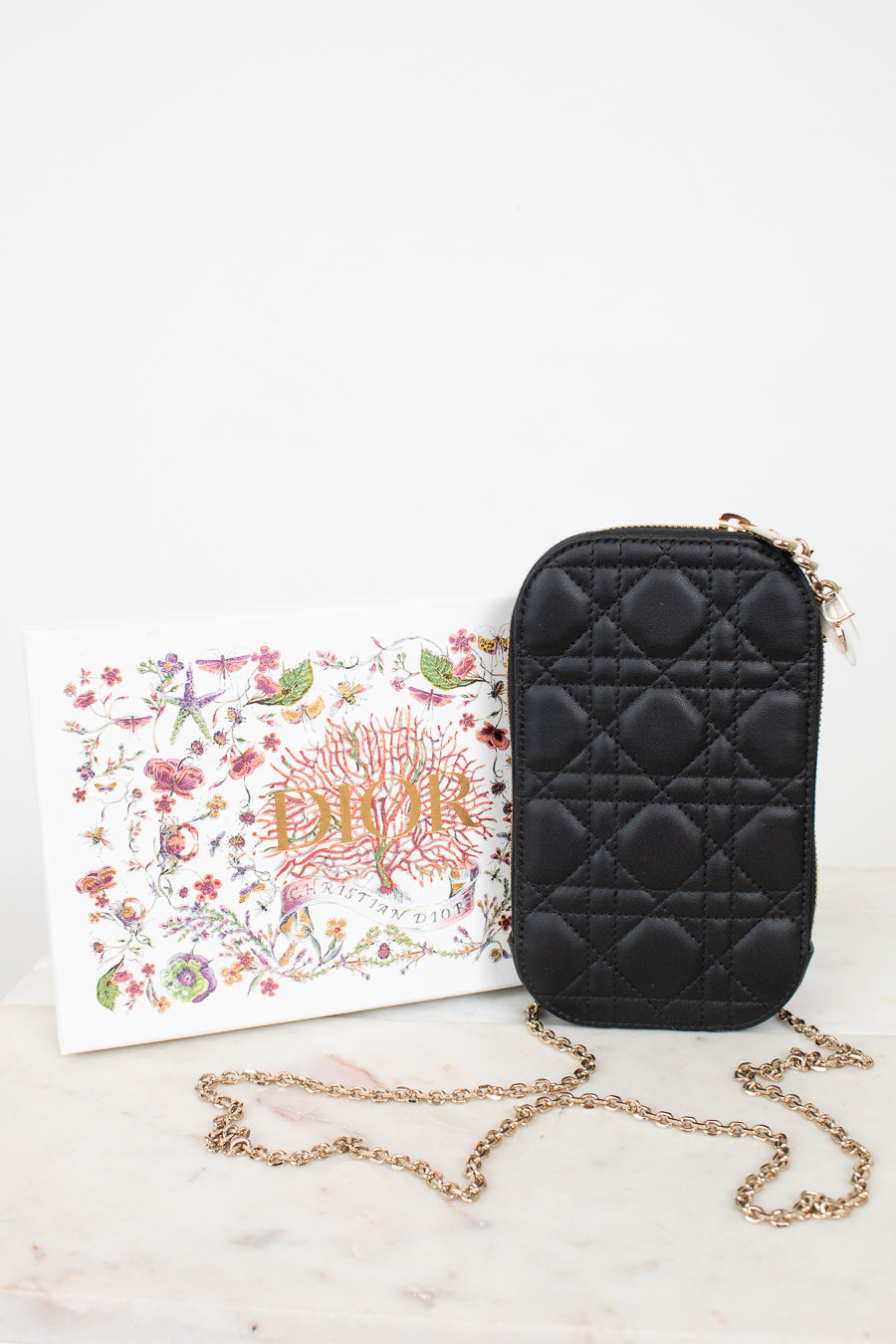 Black quilted handbag with gold chain on a white surface with a floral box.