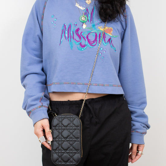 Person wearing a blue sweatshirt with colorful text and holding a black crossbody bag.
