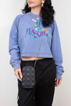Person wearing a blue sweatshirt with colorful text and holding a black crossbody bag.