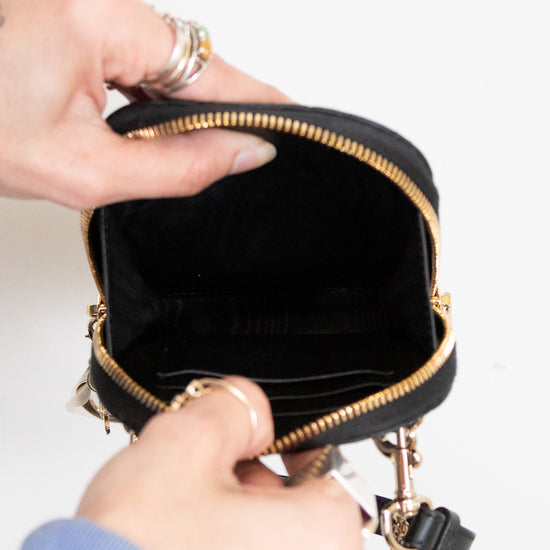 Person opening a black handbag with gold accents on a light background