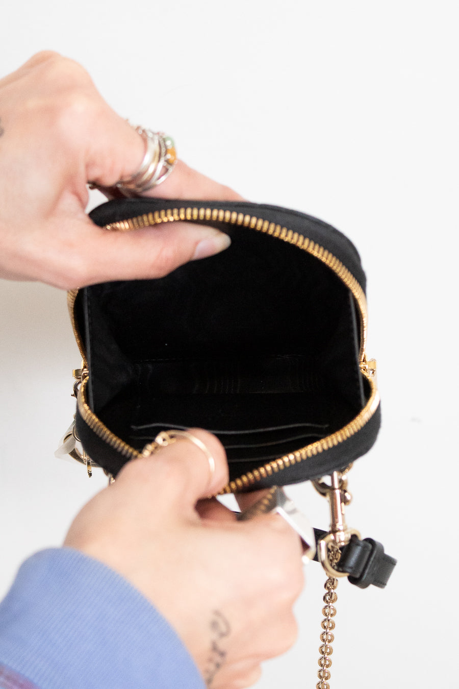 Person opening a black handbag with gold accents on a light background