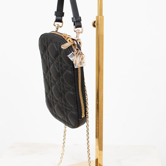 Black quilted handbag with gold chain on a gold stand against a white background