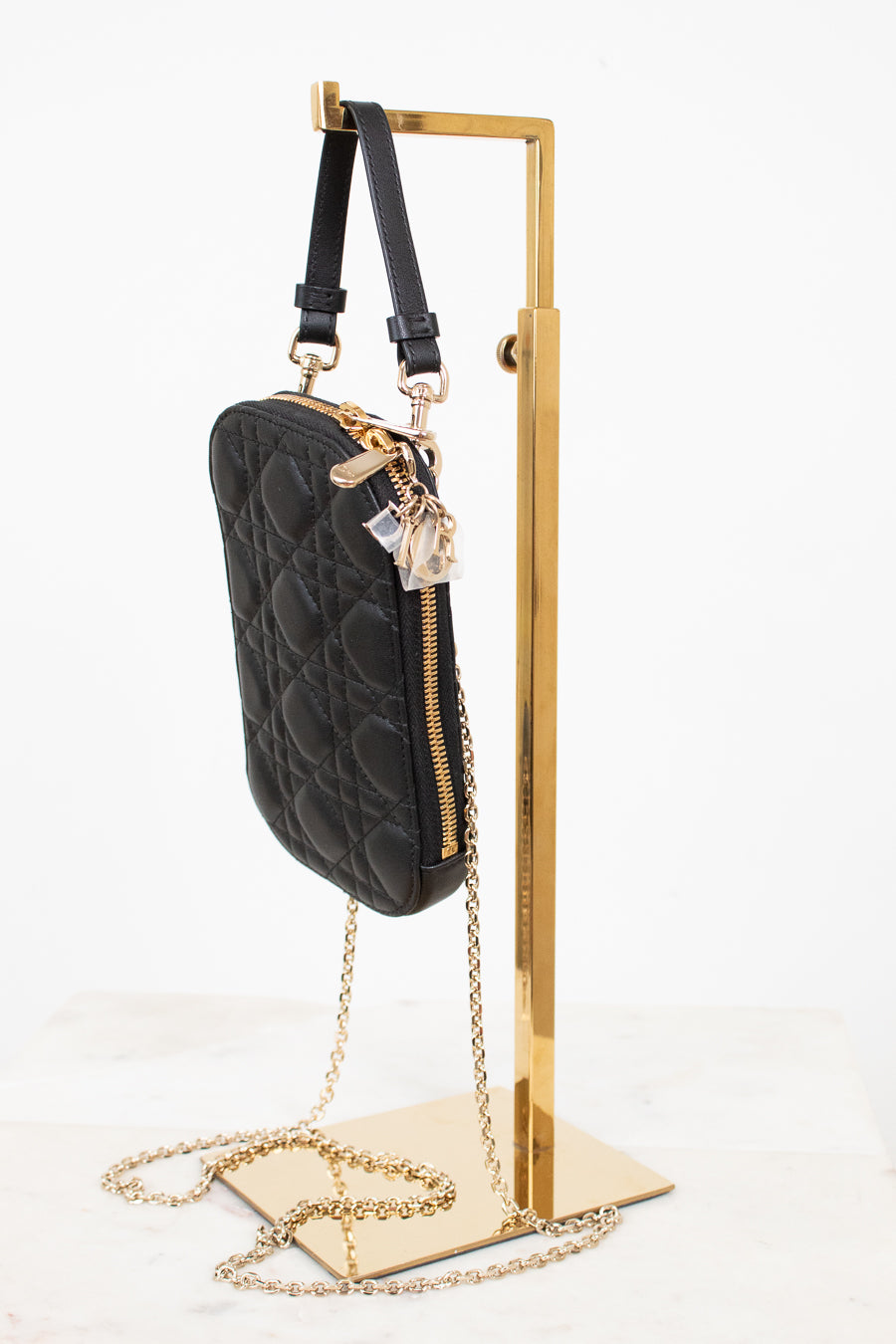 Black quilted handbag with gold chain on a gold stand against a white background