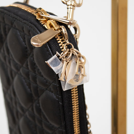 Black quilted handbag with gold zipper and decorative charm on a white background