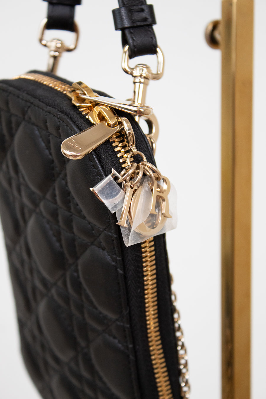 Black quilted handbag with gold zipper and decorative charm on a white background