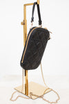 Black quilted handbag with gold chain on a stand against a white background
