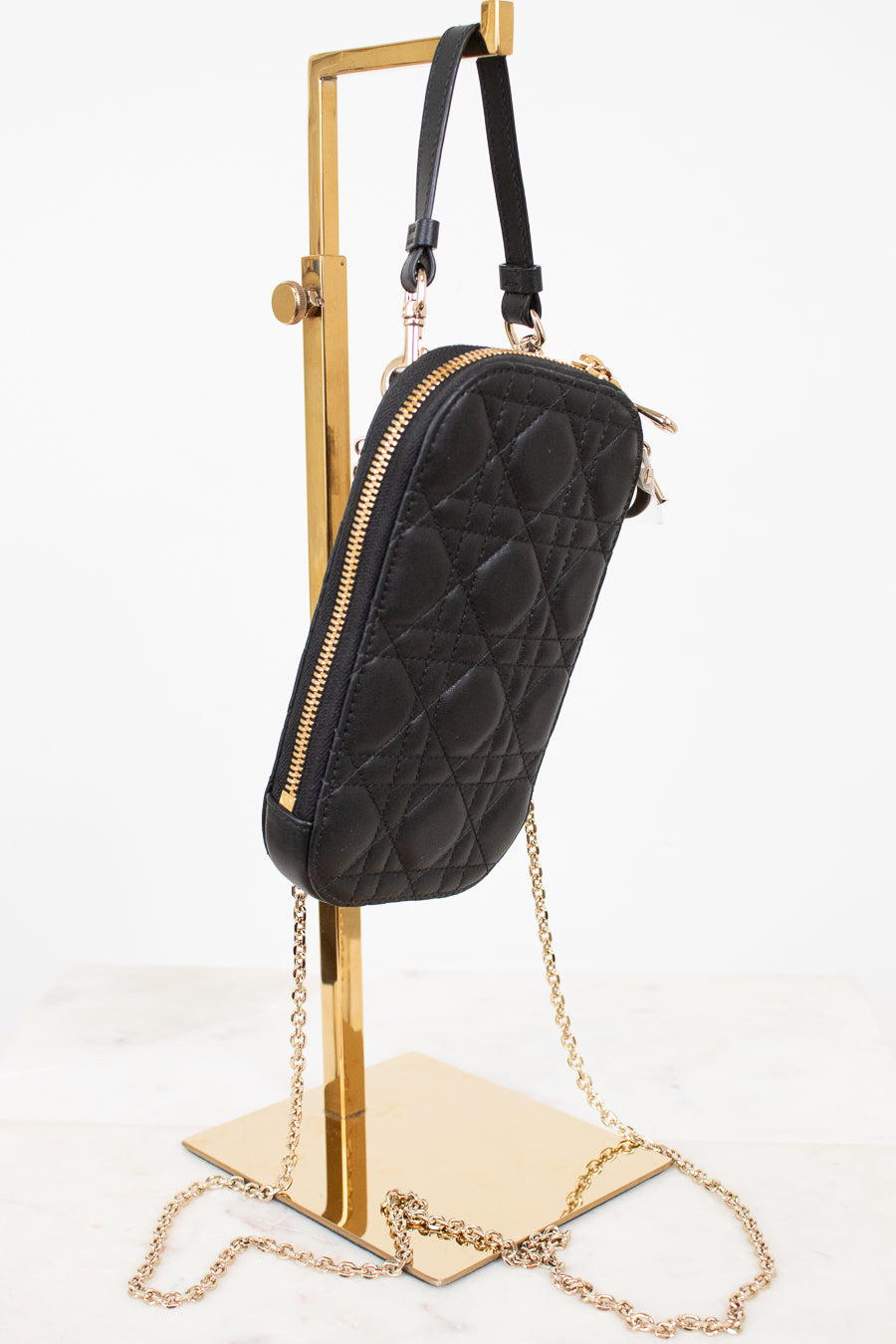 Black quilted handbag with gold chain on a stand against a white background
