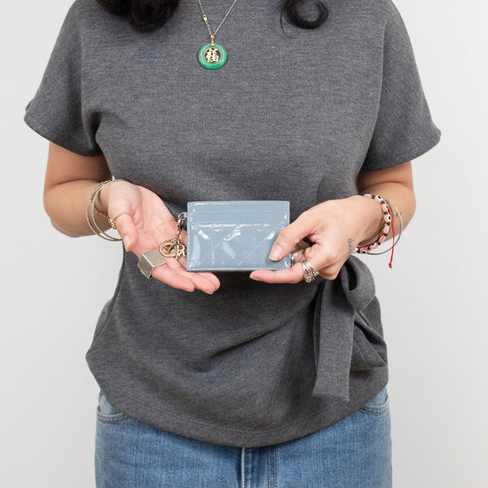 A woman wearing a heather gray short-sleeve t-shirt with a side tie detail, paired with blue jeans. She is holding a small light blue card holder in front of her torso.