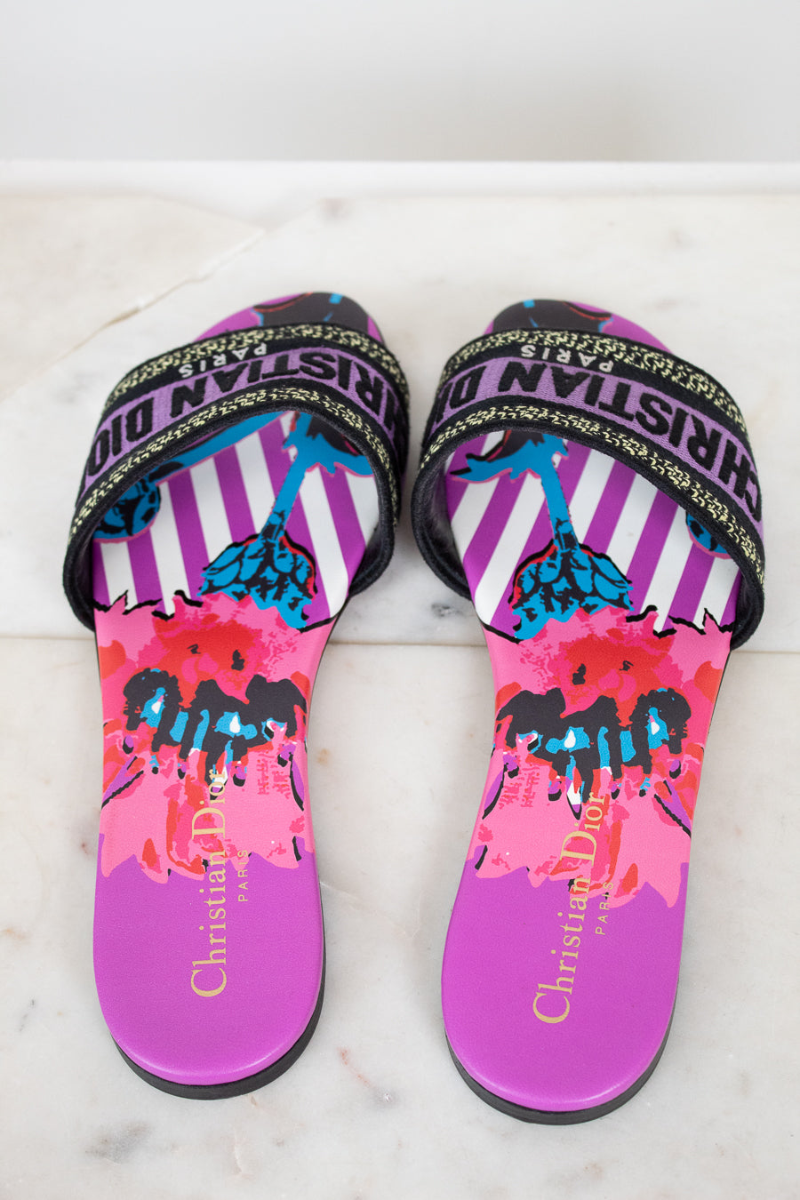 Pair of colorful sandals with 'Christian Dior' branding on a marble background