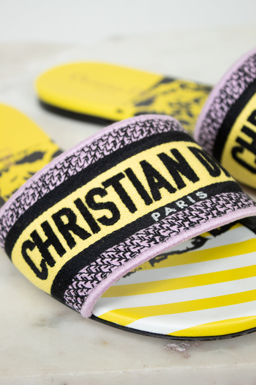 Close up of Christian Dior slides with yellow and  black  with white striped pattern on a marble background