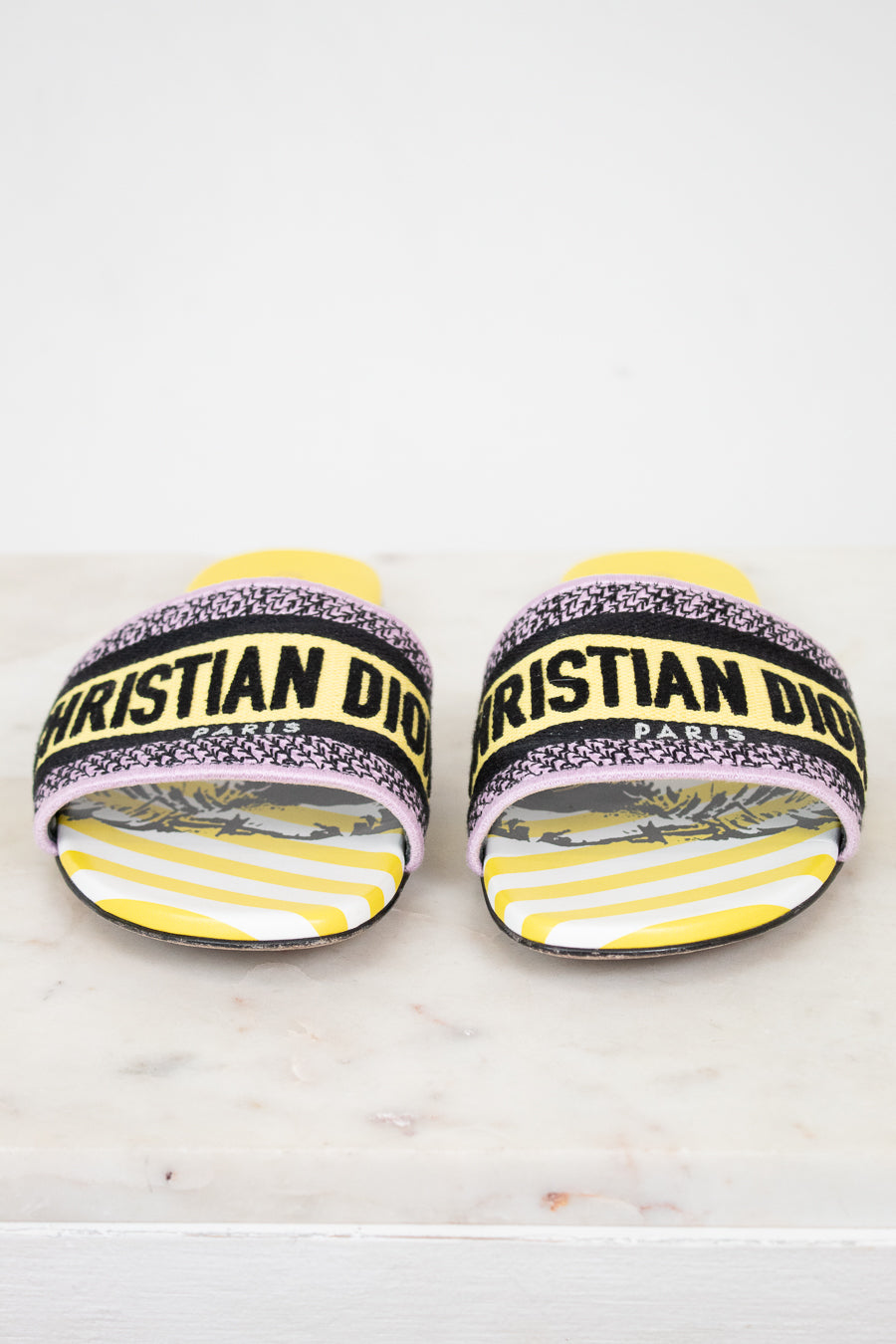 Front view of Christian Dior woven strap slides with yellow and  black  with white striped pattern on a white and marble background