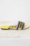 Side view of Christian Dior slides with yellow and  black  with white striped pattern on a white and marble background