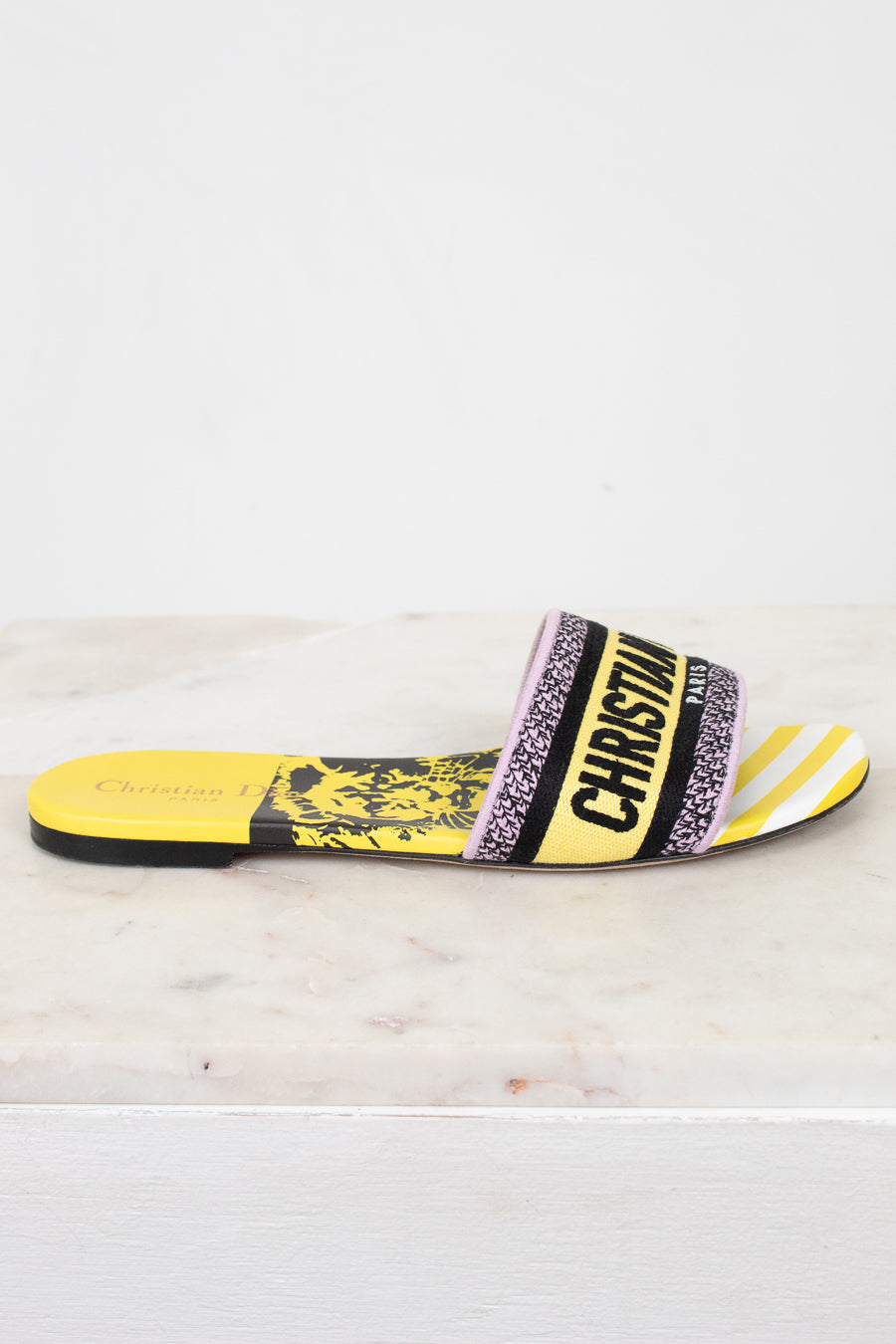 Side view of Christian Dior slides with yellow and  black  with white striped pattern on a white and marble background